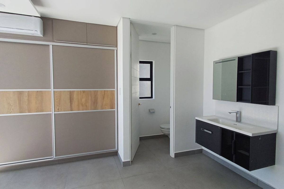 Modern bedroom featuring a large built-in wardrobe, wall-mounted air conditioning, and an en-suite bathroom with a sleek floating vanity and mirrored cabinet.