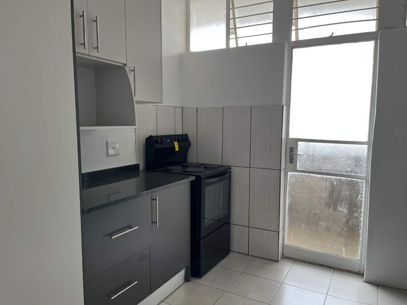 A functional kitchen featuring dark cabinetry, stone countertops, a freestanding stove, and direct access to an outdoor area through a glass panel door.