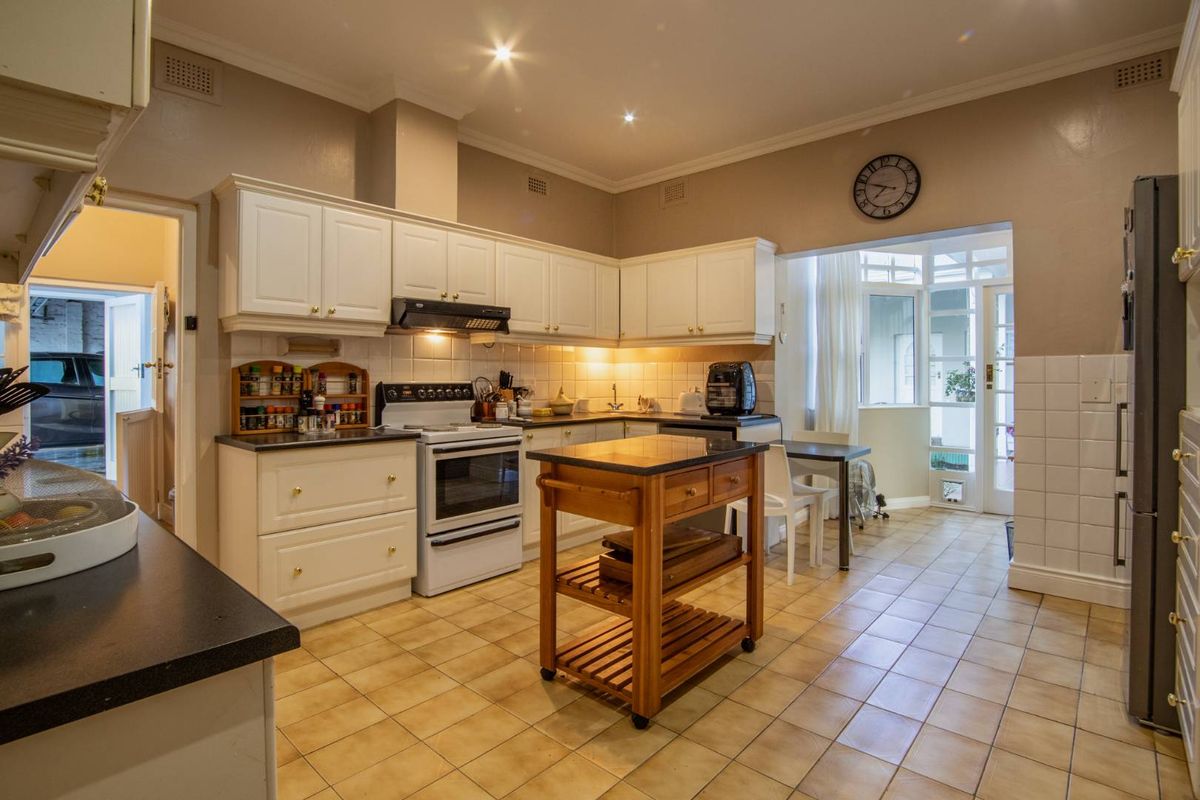 A functional kitchen featuring white cabinetry, tiled flooring, a tiled backsplash, and an integrated extractor fan, with an adjacent sunlit breakfast area.