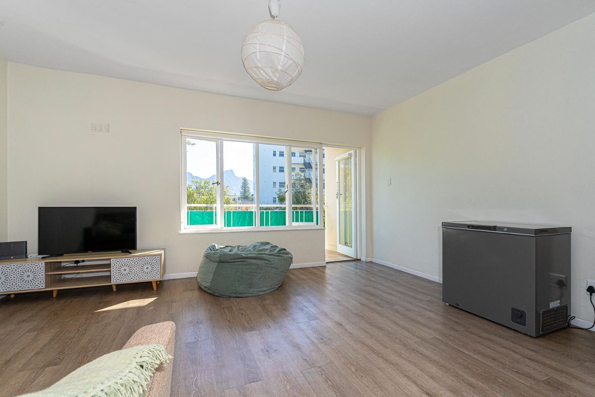 A bright living room featuring wood-look flooring, large windows, and direct access to a private balcony.