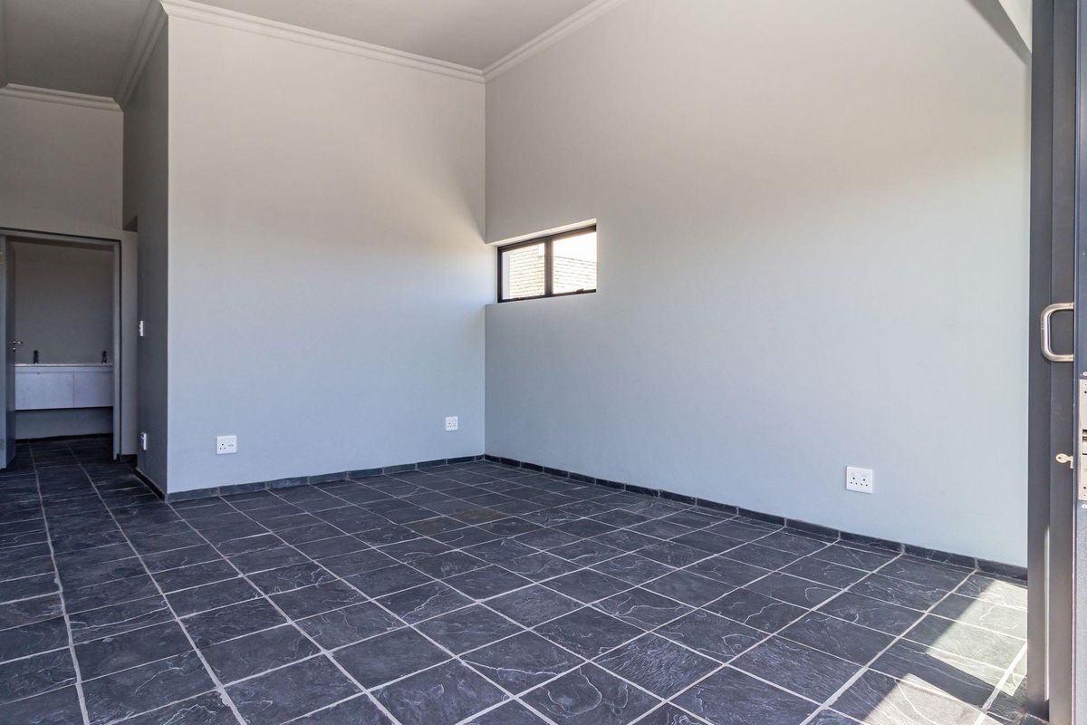 An empty living area featuring dark slate floor tiles, neutral grey walls, and a sliding glass door leading to an outdoor space.