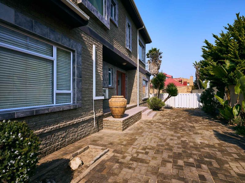 A well-maintained rear exterior view featuring brick paving, a solid brick facade, and established garden landscaping.