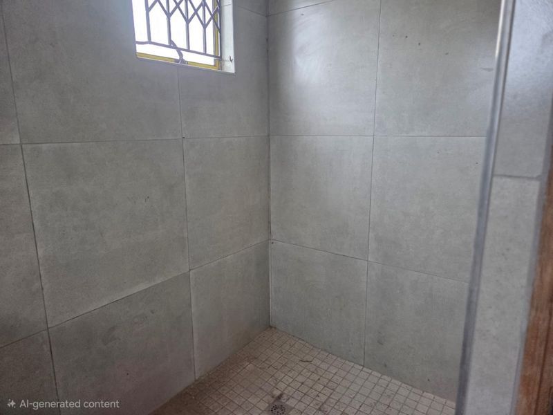 A tiled shower enclosure featuring a small window with a security grille and a floor drain.