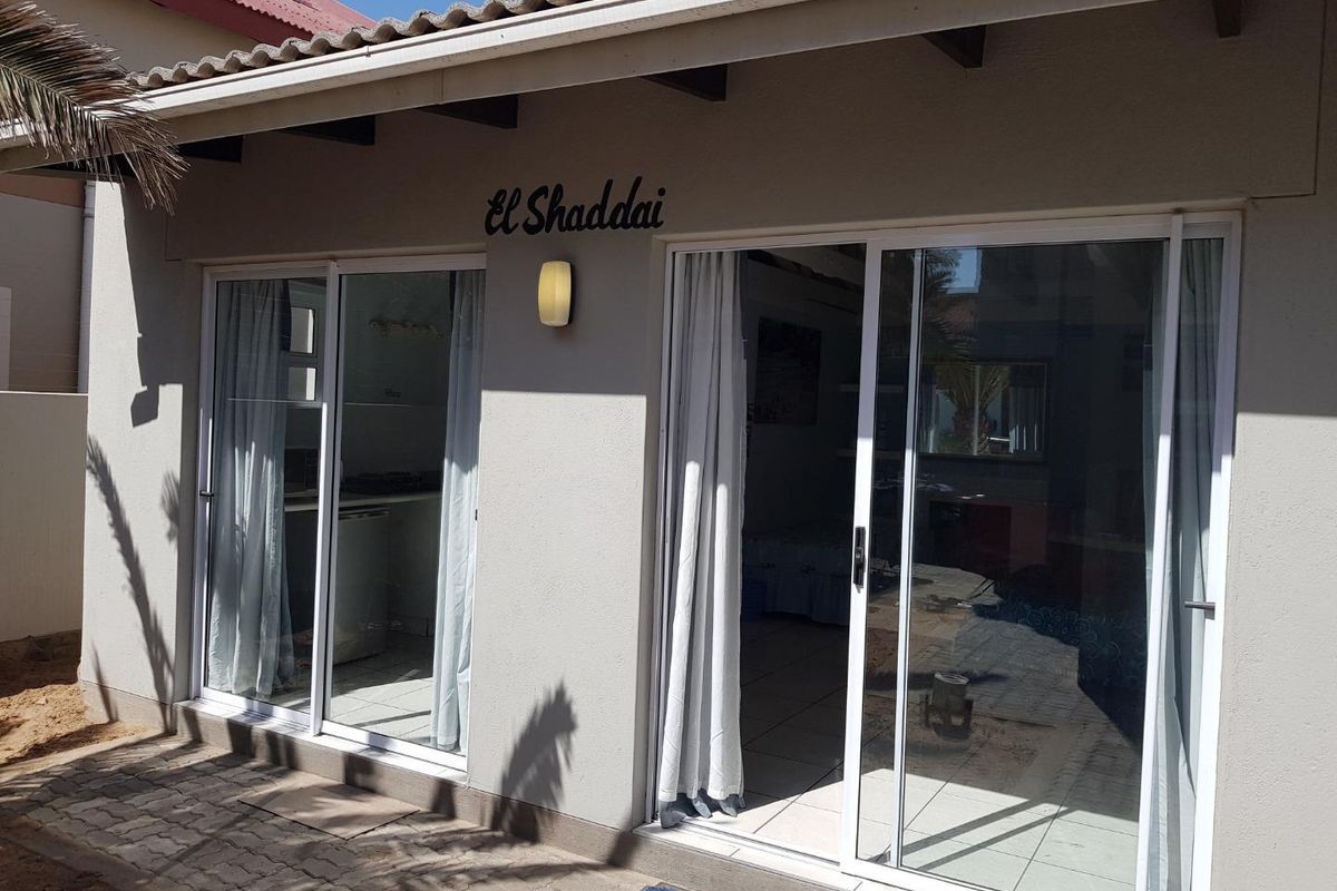Exterior view of a guest house unit featuring sliding glass doors, tiled patio area, and exposed roof rafters.