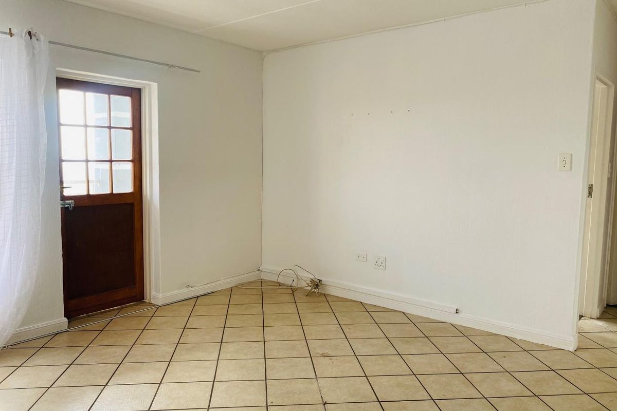 An empty living room featuring tiled flooring and a timber-framed glass door leading to the exterior.