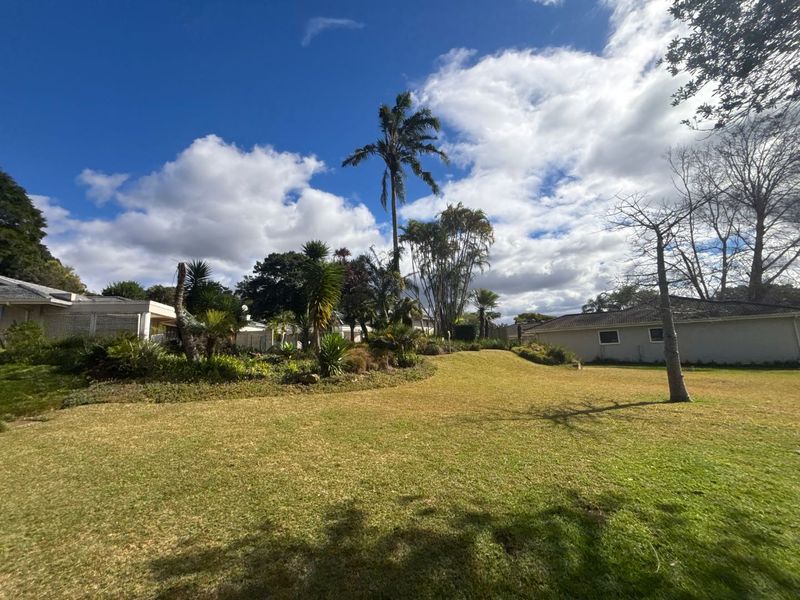 A spacious, well-maintained garden featuring a large lawn area, mature trees, and established landscaping surrounding the townhouse property.