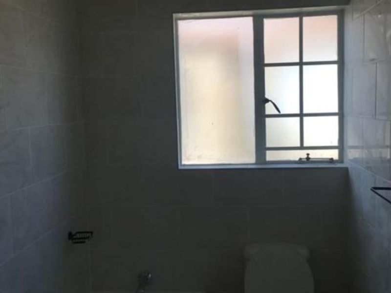 A functional bathroom featuring a bathtub, toilet, and tiled walls, illuminated by a window with security bars.