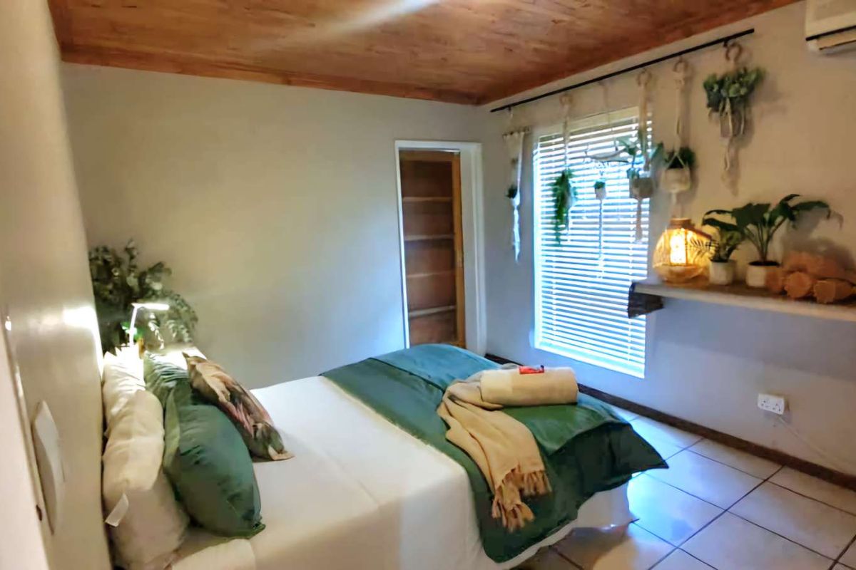 A cozy bedroom featuring a warm timber-clad ceiling, tiled flooring, and a wall-mounted air conditioning unit.