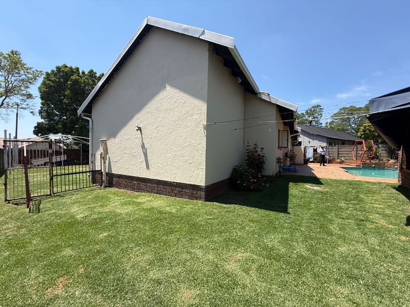 Rear view of the property featuring a well-maintained lawn, a swimming pool, and a paved patio area adjacent to the house structure.