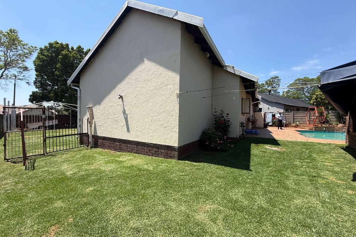 Rear view of the property featuring a well-maintained lawn, a swimming pool, and a paved patio area adjacent to the house structure.