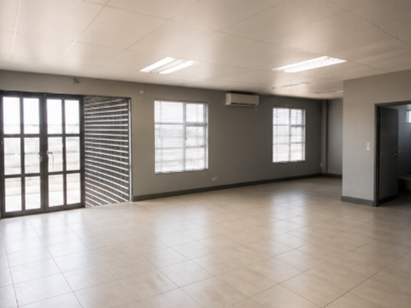 Spacious open-plan industrial office area featuring neutral tiled flooring, suspended ceilings, integrated air conditioning, and ample natural light through aluminium-framed windows.