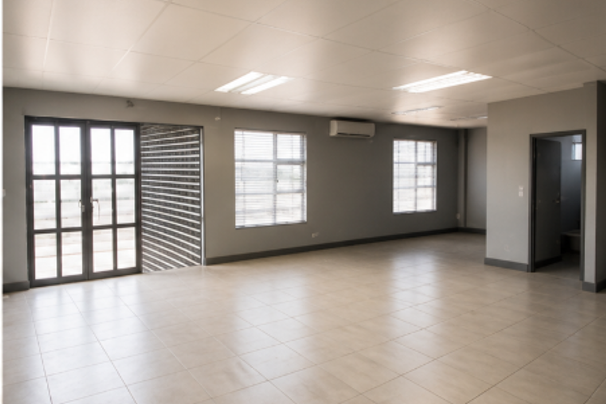 Spacious open-plan industrial office area featuring neutral tiled flooring, suspended ceilings, integrated air conditioning, and ample natural light through aluminium-framed windows.