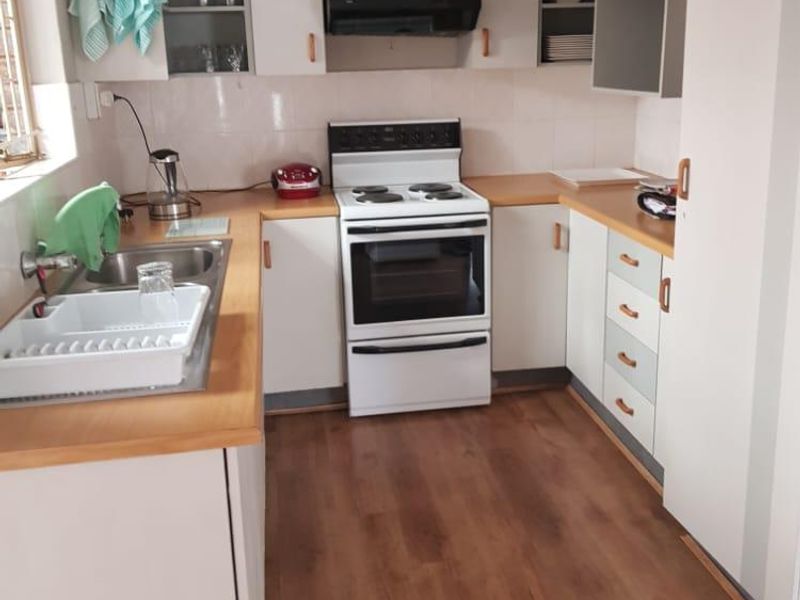 A functional kitchen featuring laminate countertops, built-in cabinetry, a freestanding electric stove with extractor fan, and durable laminate flooring.