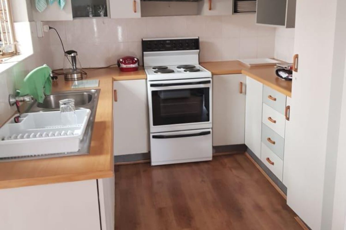 A functional kitchen featuring laminate countertops, built-in cabinetry, a freestanding electric stove with extractor fan, and durable laminate flooring.