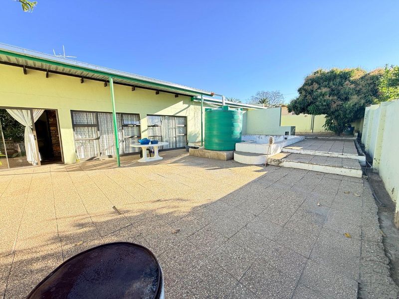 Rear exterior area featuring a paved patio, concrete steps, and a water storage tank, with potential for landscaping and surface improvements.