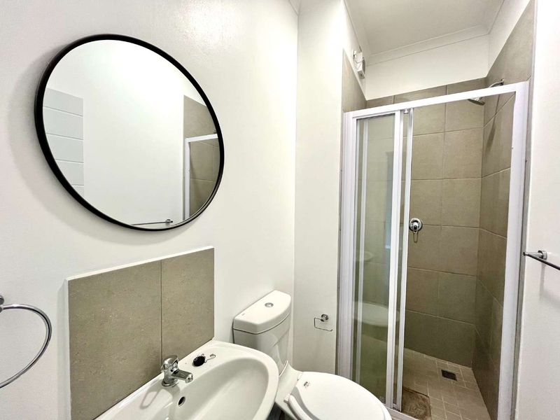 A clean, functional bathroom featuring a shower enclosure, pedestal basin, toilet, and neutral wall tiling.