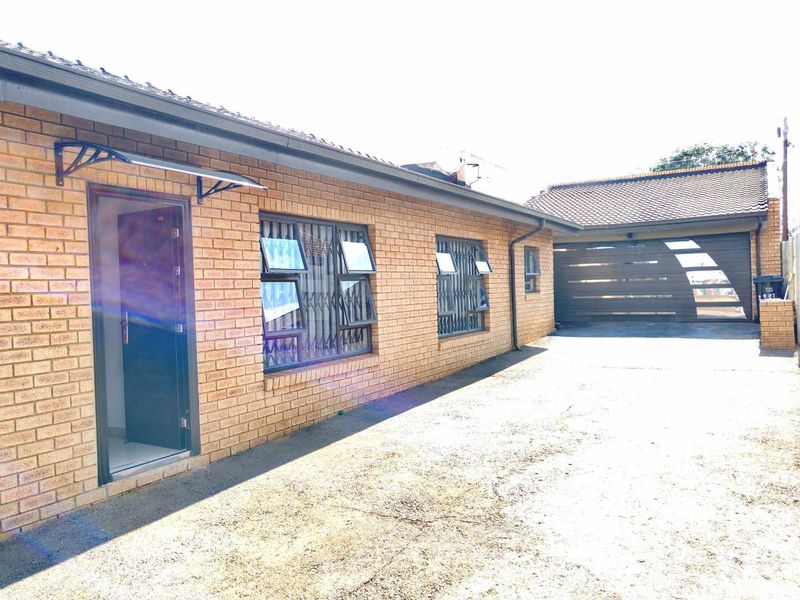 A well-maintained face brick exterior featuring a paved driveway, secure window bars, and an attached garage.