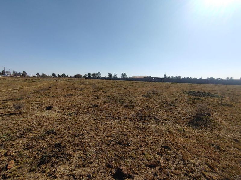 A wide-angle view of a vacant agricultural land plot featuring dry grass and a perimeter boundary wall in the distance.