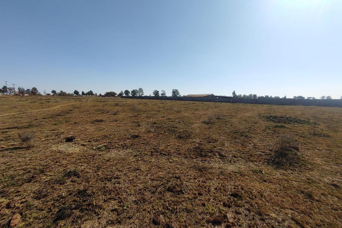 A wide-angle view of a vacant agricultural land plot featuring dry grass and a perimeter boundary wall in the distance.