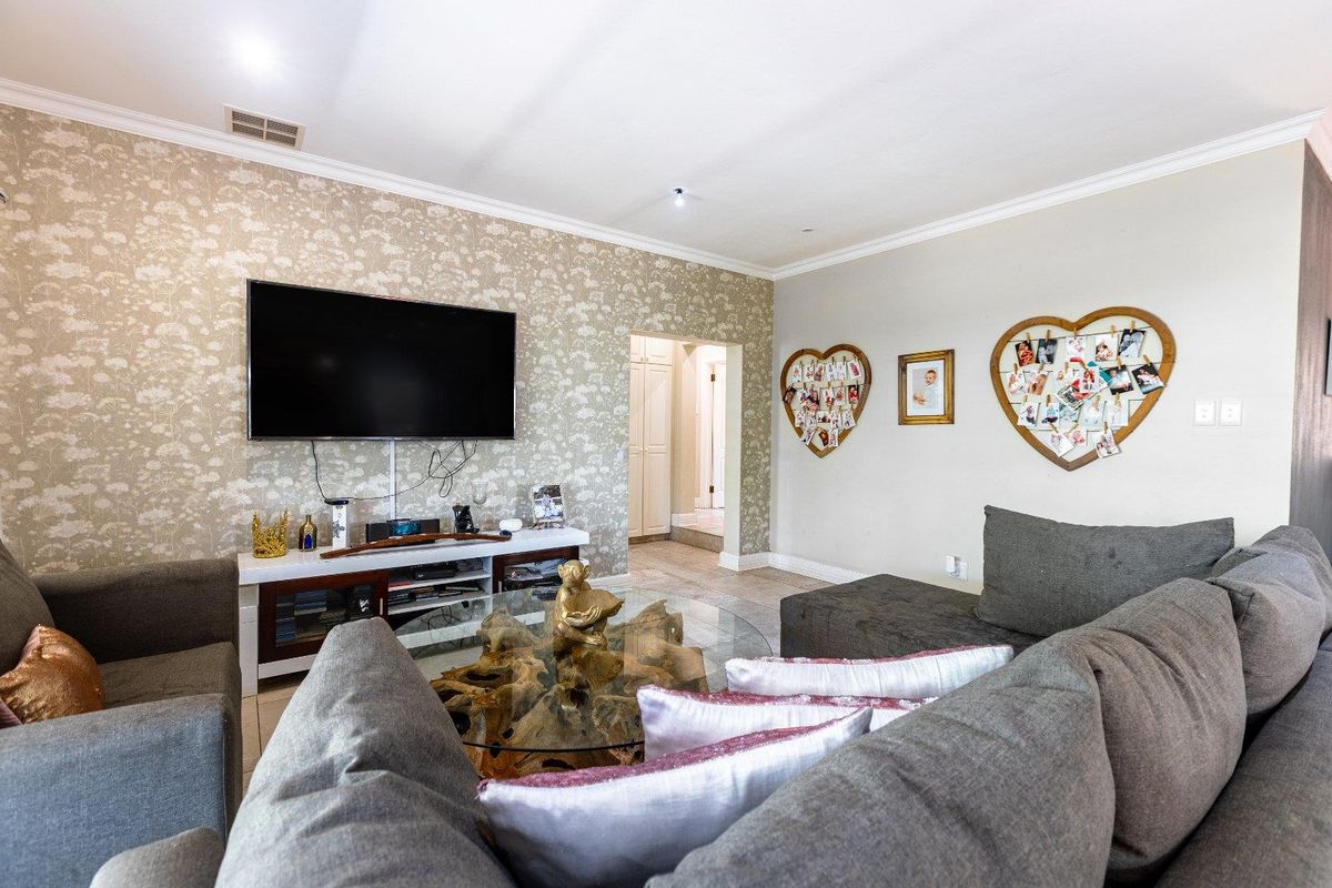 A comfortable living room featuring patterned wallpaper, recessed ceiling lighting, and tiled flooring, with a clear view into the adjacent hallway.