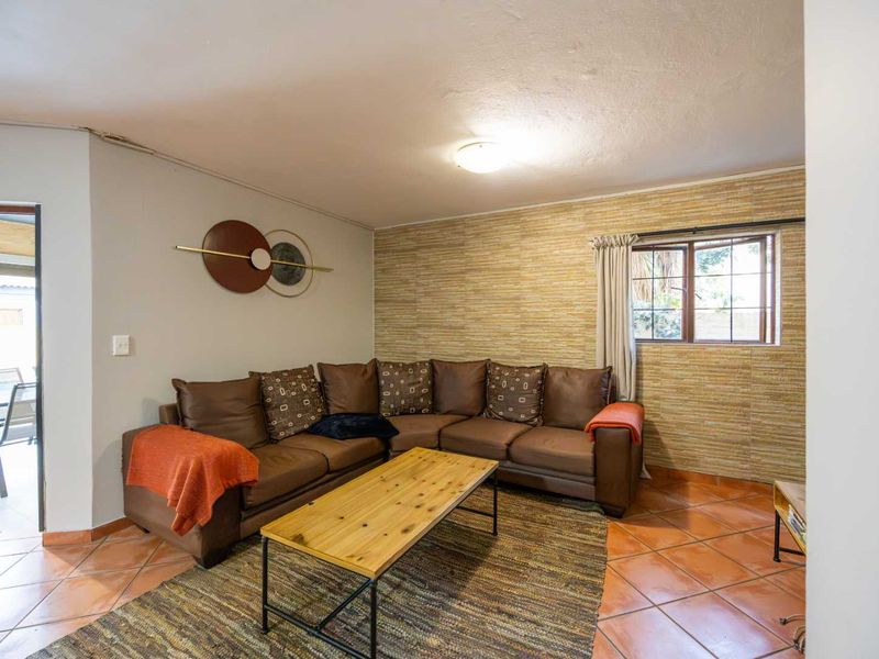 A living room featuring terracotta floor tiles, a textured feature wall, and a window with security bars, offering a functional and lived-in space.