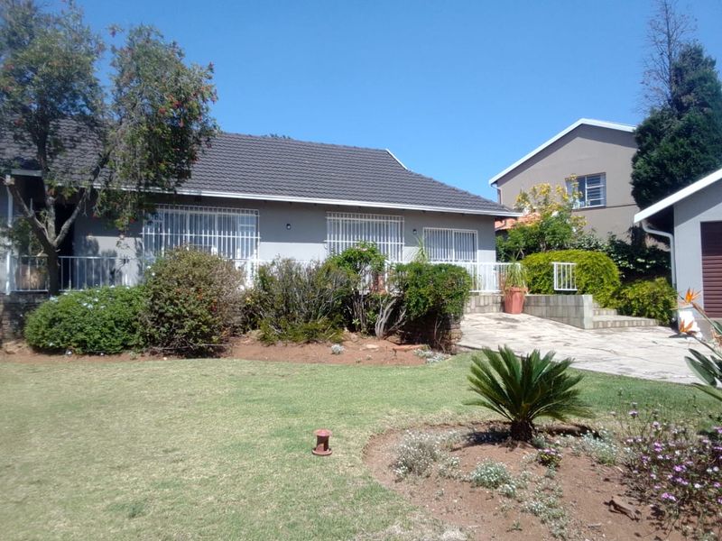 Rear view of the house featuring a tiled roof, security bars on windows, a paved driveway, and a well-maintained garden area.