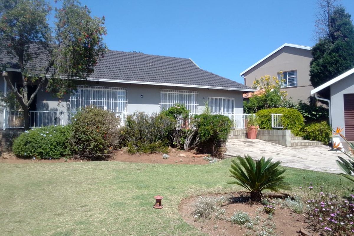 Rear view of the house featuring a tiled roof, security bars on windows, a paved driveway, and a well-maintained garden area.