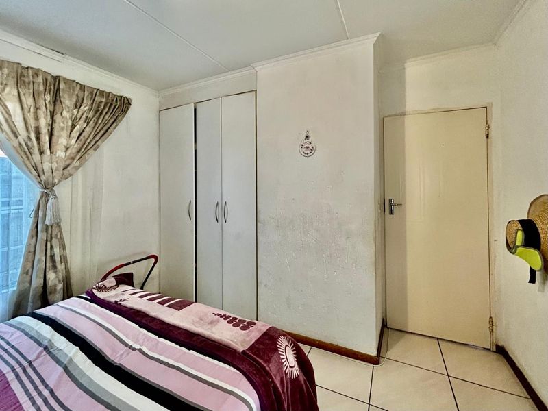 A bedroom featuring tiled flooring, a built-in wardrobe, and an internal door, requiring cosmetic updates to the wall surfaces.