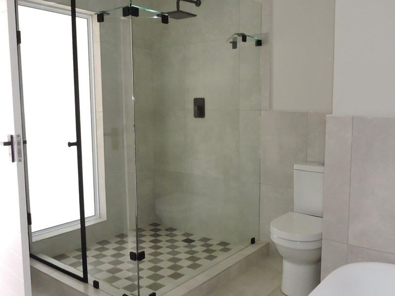 Modern bathroom featuring a walk-in shower with glass enclosure, rain shower head, and contemporary black matte fixtures with neutral wall and floor tiling.