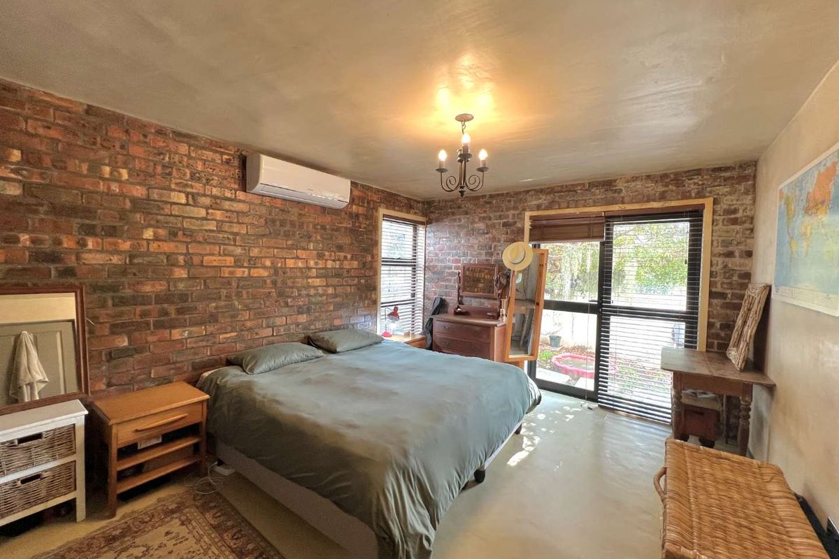 Spacious bedroom featuring exposed brick walls, a split-system air conditioner, and a sliding glass door providing direct access to the outdoor area.