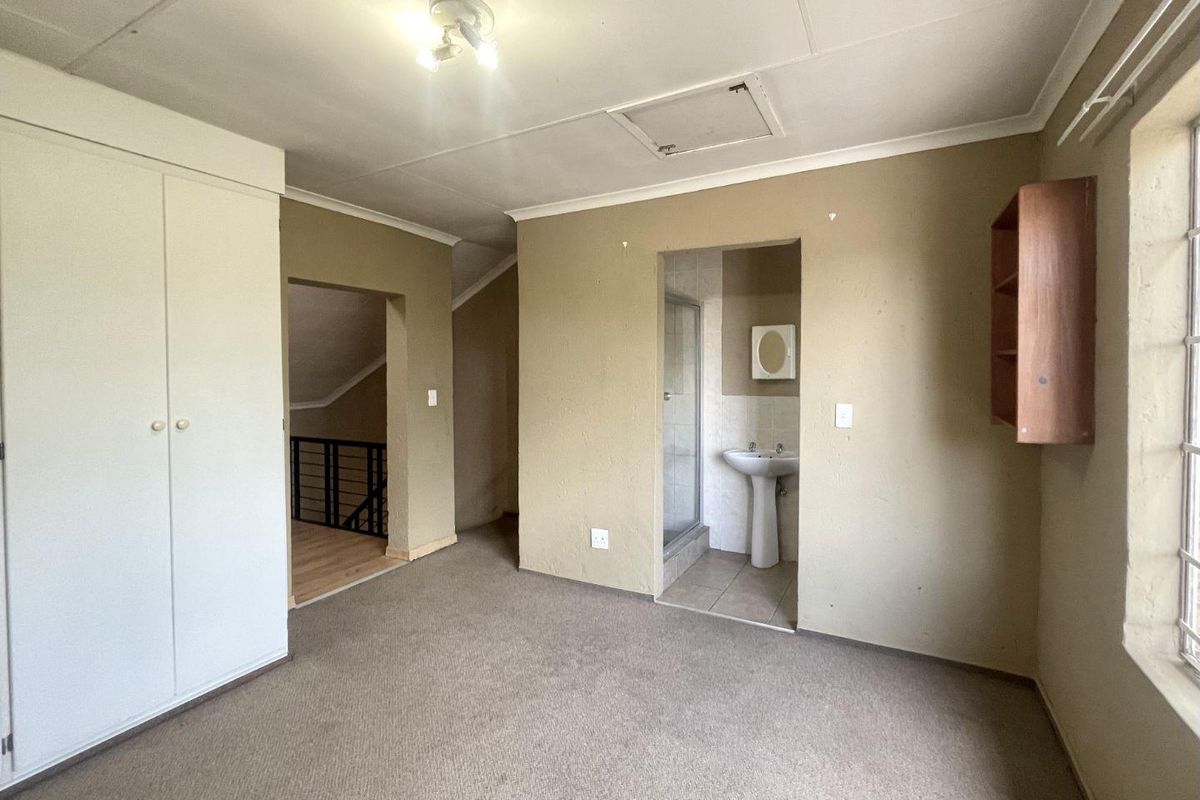 A bedroom featuring built-in cupboards and an en-suite bathroom with a pedestal basin and shower enclosure.