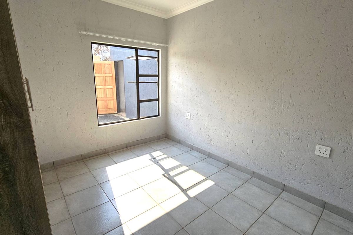 A bright, empty bedroom featuring tiled flooring, textured walls, and a window providing natural light.