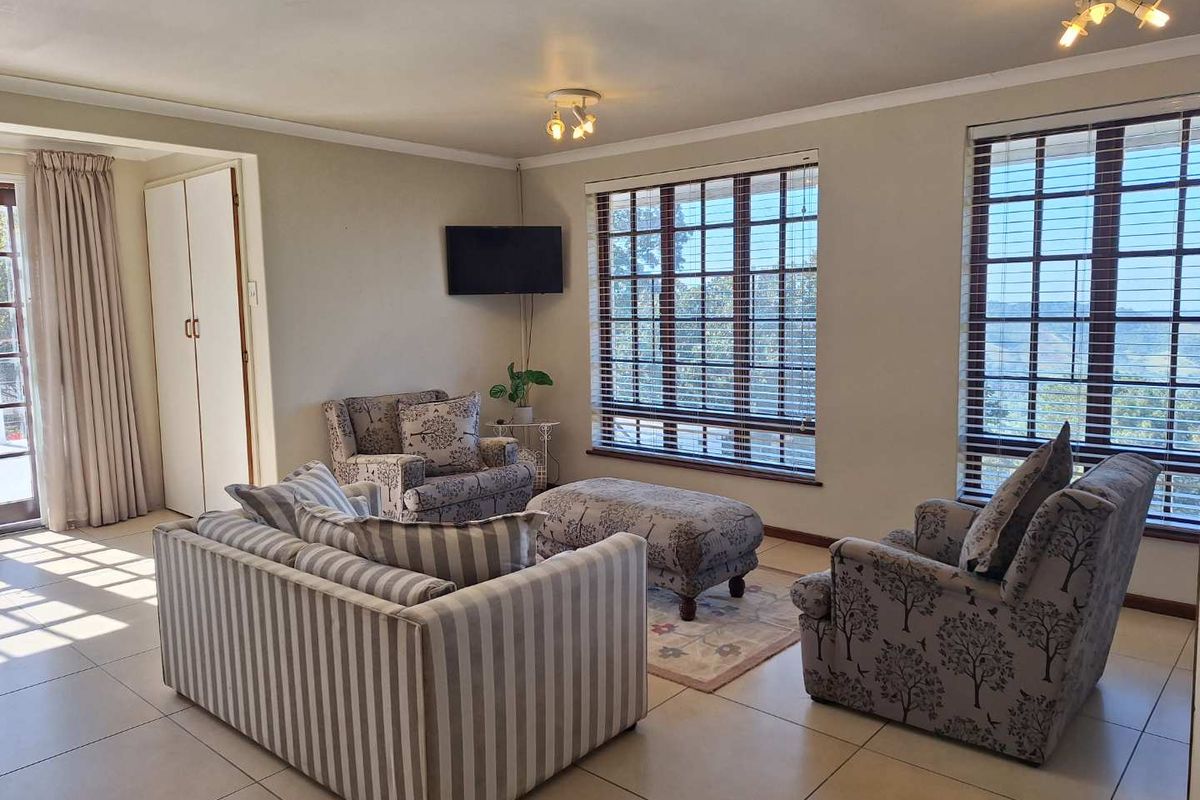A bright and spacious living room featuring large windows with venetian blinds, tiled flooring, and a built-in storage cupboard.