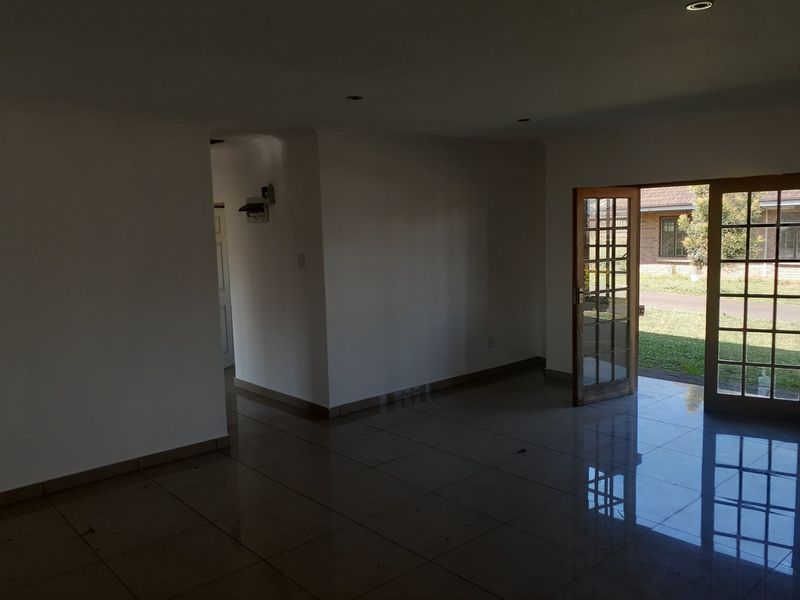 An empty, open-plan living area featuring polished tiled flooring, recessed lighting, and wooden-framed glass doors providing direct access to the garden.