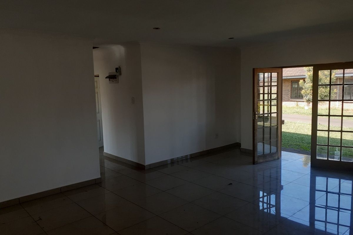 An empty, open-plan living area featuring polished tiled flooring, recessed lighting, and wooden-framed glass doors providing direct access to the garden.