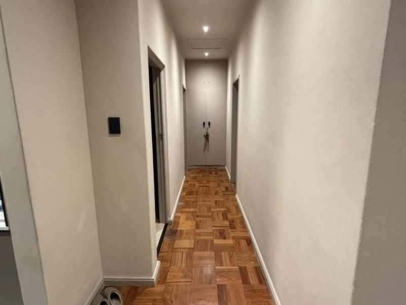 A clean, well-lit hallway featuring classic parquet wood flooring and a built-in storage cupboard at the end of the corridor.