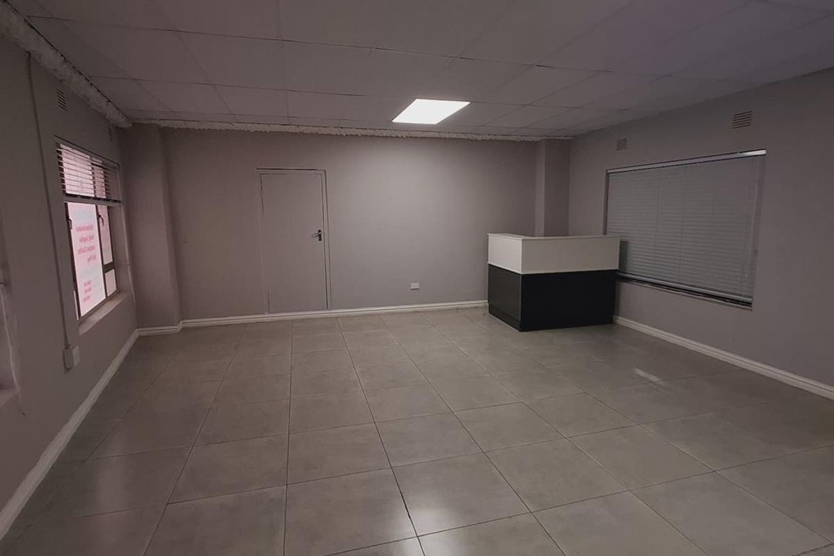 A spacious, empty office area featuring neutral tiled flooring, a built-in reception counter, and recessed ceiling lighting, ready for professional use.