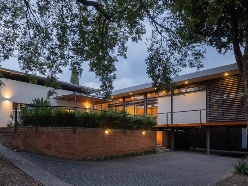 Modern architectural home featuring a brick retaining wall, paved driveway, and elevated timber deck with integrated exterior lighting.