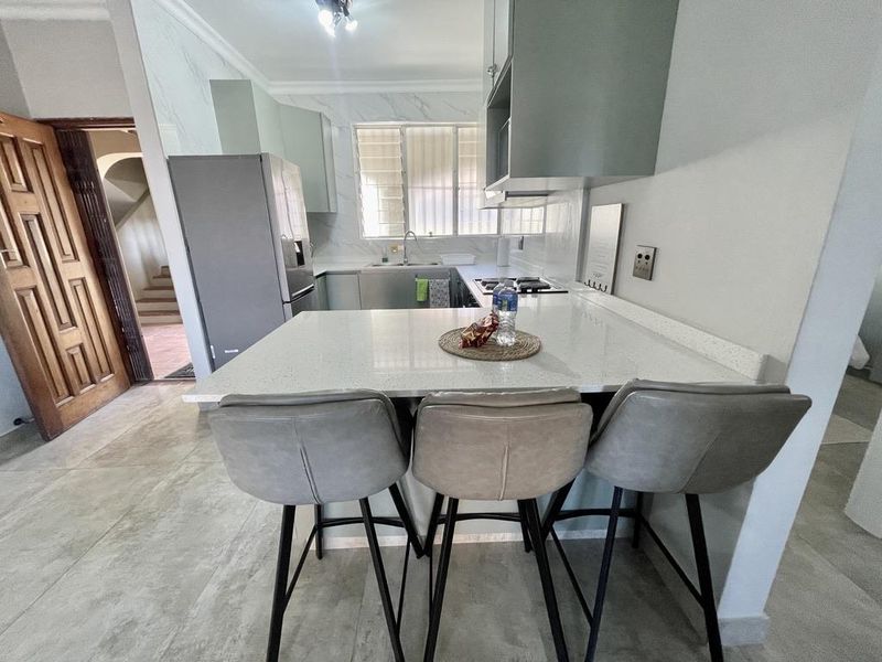 Modern kitchen featuring quartz countertops, built-in cabinetry, gas hob, extractor fan, and tiled flooring with a breakfast bar area.