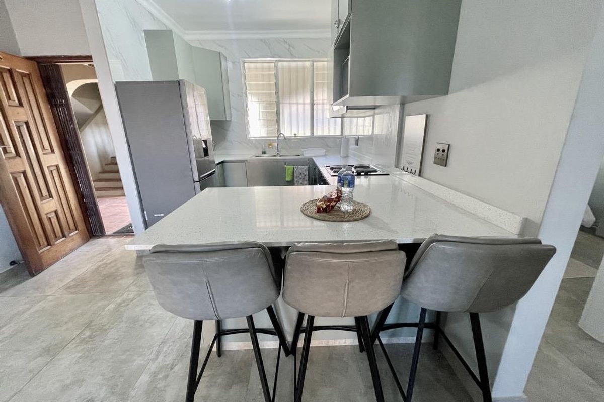 Modern kitchen featuring quartz countertops, built-in cabinetry, gas hob, extractor fan, and tiled flooring with a breakfast bar area.