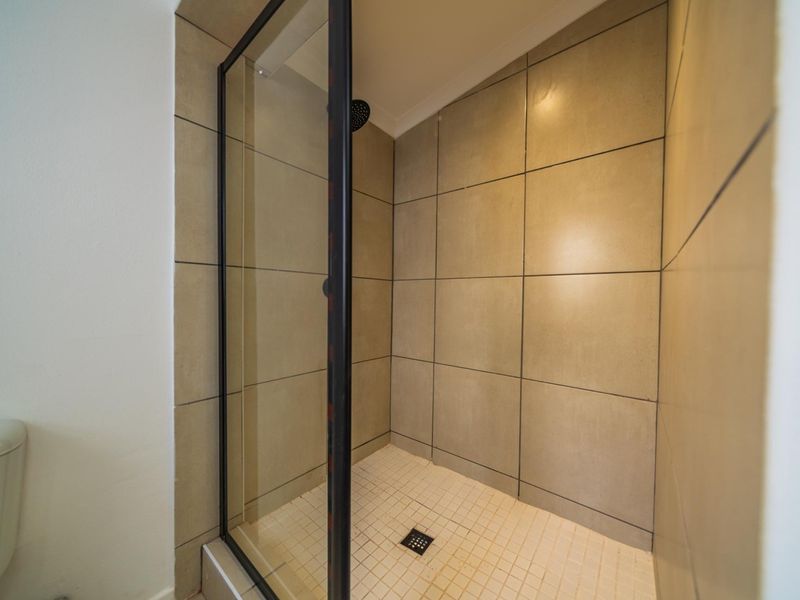 A functional bathroom featuring a walk-in shower with a glass enclosure, neutral wall tiling, and a separate toilet.