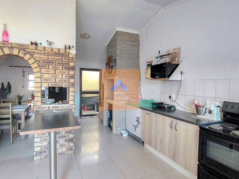 Kitchen featuring tiled flooring, laminate cabinetry, a tiled backsplash, and a distinctive brick archway leading to an adjacent living area.