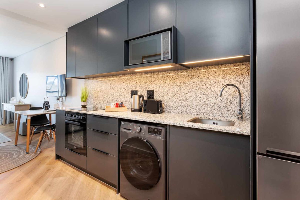 Modern kitchen featuring dark cabinetry, granite countertops, integrated appliances, and under-cabinet lighting, seamlessly flowing into the adjacent dining area.
