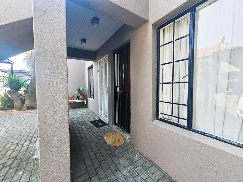 A covered entrance area featuring a paved walkway, security gate, and window burglar bars, providing a secure and functional access point to the apartment.