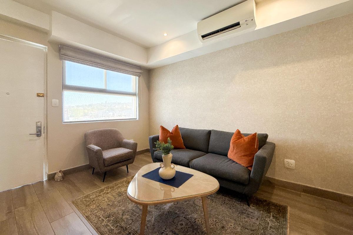 A well-maintained living room featuring tiled flooring, a wall-mounted split-system air conditioner, and a large window with a roller blind.