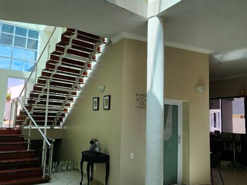 Spacious double-volume entrance hall featuring a large skylight, modern staircase with glass balustrades, and polished tiled flooring.