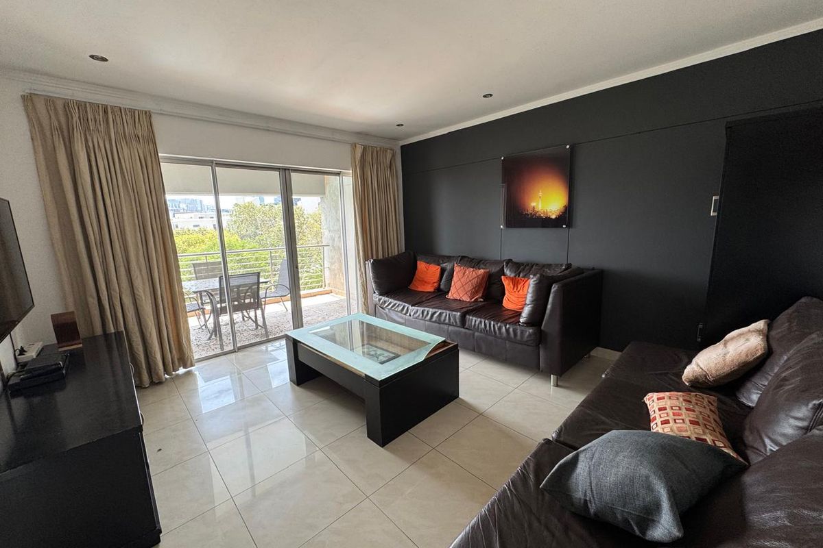 Spacious living room featuring large format floor tiles, a dark accent wall, and direct access to a private balcony through sliding glass doors.