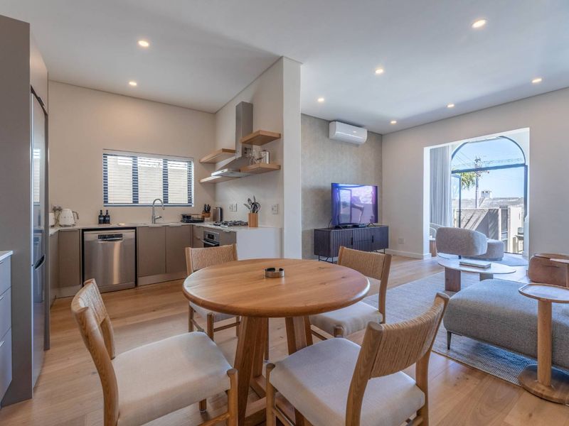 Modern open-plan living area featuring a sleek kitchen with integrated appliances, timber flooring, recessed lighting, and seamless access to an arched balcony.
