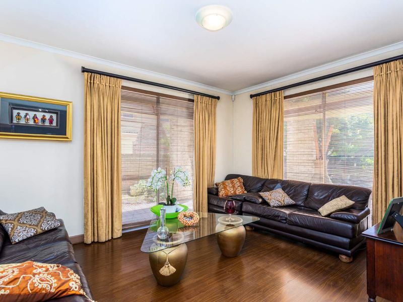 A well-lit living room featuring dark laminate flooring, large windows with venetian blinds, and neutral wall finishes.