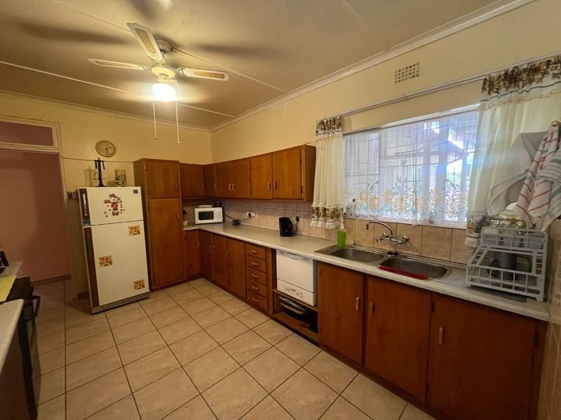 A functional kitchen featuring wooden cabinetry, tiled flooring, a double basin sink, and a ceiling fan, offering a classic layout with potential for modernization.